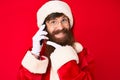 Handsome young red head man with long beard wearing santa claus costume talking on the phone smiling happy pointing with hand and Royalty Free Stock Photo