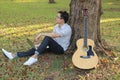 Handsome young relaxed man sitting on green grass and happiness with laptop against acoustic guitar in the park outdoors Royalty Free Stock Photo