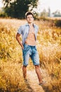 A handsome young man with a strong muscular torso in an unbuttoned shirt is standing on a meadow in nature outside city Royalty Free Stock Photo