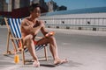 handsome young shirtless man sitting on sun lounger and applying sunscreen lotion Royalty Free Stock Photo