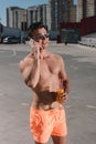 handsome young shirtless man in swimming shorts with cocktail talking by phone Royalty Free Stock Photo