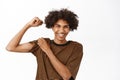 Handsome young slim boy, laughing and showing biceps, flexing muscles, standing over white background Royalty Free Stock Photo