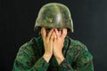 Handsome young soldier wearing uniform suffering from stress, using both hands to cover his face, in a black background Royalty Free Stock Photo