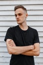 Handsome young stylish man with a stylish hairstyle in a fashionable black t-shirt posing against a wooden vintage wall background Royalty Free Stock Photo