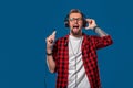 Handsome young stylish man in headphones holding MP3 Player and dancing while standing against blue background Royalty Free Stock Photo
