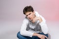 Handsome young stylish man sitting on the floor in studio. Teenager model posing while sitting on a pink background in casual Royalty Free Stock Photo