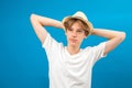 Handsome young teen boy with handsbehinde his head isolated on blue. Friendly well-looking boy spending time in dreaming