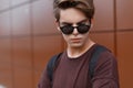 Handsome young teenager man in fashion sunglasses with a hairstyle in a summer fashionable t-shirt on the street. Royalty Free Stock Photo