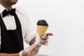 Handsome waiter in elegant classic suit serving trendy dessert, black ice cream in waffle cone. Uninsulated white Royalty Free Stock Photo