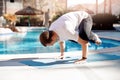 Handstand asana meditation yoga caucasian man in white shirt on background pool, palm trees and sunlight