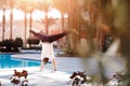 Handstand balance asana meditation yoga caucasian man in white shirt on background pool, palm trees and sunlight