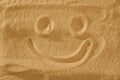 Handwrited face on the sand at the beach. Symbol smile on beach background.