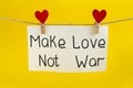 Handwriting inscription "make love not war" suspended on clips in form of the heart on the yellow background. Royalty Free Stock Photo