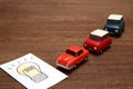 Handwritten bulb illustration and miniature cars on wood.