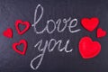 Handwritten chalk inscription I love you on black chalkboard with red decorative hearts.