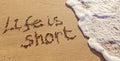 Handwritten inscription Life is Short on the sand with flushing foamy wave Royalty Free Stock Photo