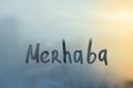 lettering Merhaba in Turkish is hello in english paint with finger with streaks of water on splashed by rain foggy glass Royalty Free Stock Photo