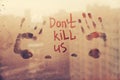 Message call Dont kill us and two handprint are painted handwriting on brown window with raindrops