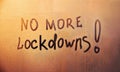 Message, No more lockdowns are painted handwriting on wet orange glass of sunset window in light of city