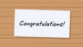A handwritten message saying Congratulations written on a piece of white paper attached to a wooden background Royalty Free Stock Photo
