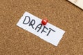A handwritten note saying DRAFT pinned on a corkboard surface, serving as a reminder for ongoing projects or tasks at a Royalty Free Stock Photo