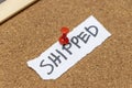 A handwritten note saying SHIPPED is pinned to a corkboard with a red pushpin. This visual representation signifies the Royalty Free Stock Photo