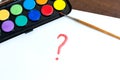 Handwritten question mark with brush and watercolor paints on white background. Box of watercolor paints with a brush for drawing Royalty Free Stock Photo