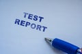Handwritten text spelling out TEST REPORT on a blank white sheet with a blue pen beside it, ideal for documentation or a Royalty Free Stock Photo