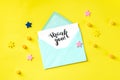 Handwritten Thank You post card in a teal blue envelope, shot from the top on a yellow background