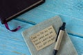 Handwritten verse on a note with a pen and closed Holy Bible Book on a blue wooden background