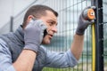 handy man measuring fence while calling on phone