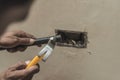 A handyman adjusting a hole in the wall with a chisel and hammer to insert a junction box. Replacing a faulty electrical outlet