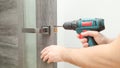 Handyman Fitting A New Door Using A Screwdriver At Home. Carpenter at lock installation with electric drill into interior wood