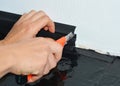 A handyman is installing a black plastic skirting board to a white wall cutting