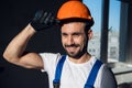 Handyman in overalls holds on to the visor of a hard hat