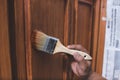 A handyman paints a fresh coat of varnish on the surface of a base kitchen cabinet with a medium sized brush. Home renovation or