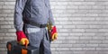 Handyman with toolbox and tool belt against brick wall background with copy space.