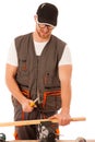 Handyman in work clothing hammering nail with hammer in home workshop.