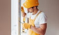 Handyman in yellow uniform installs new window. House renovation conception