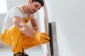 Handyman in yellow uniform polishing wall indoors. House renovation conception