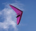 Hang glider flies by on purple wings with blue sky and wispy clouds above