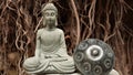A stone Buddha in the lotus position with his eyes closed meditates next to the hang drum