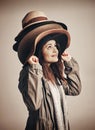 Hang on to your hats. Sale season is coming. Studio shot of a young woman wearing a pile of hats against a brown Royalty Free Stock Photo