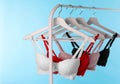 Hangers with beautiful lace bras on rack against blue. Stylish underwear