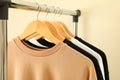 Hangers with stylish sweatshirts on beige background