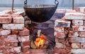 Hanging black sooty cauldron over bonfire surrounded by a brick wall, camping vacation outdoor kitchen