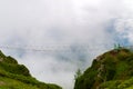 Hanging bridge over chasm in fog. Rope bridge between peaks in cloud Royalty Free Stock Photo