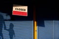 Closed sign board with sunlight and shadow of mother holding child hand walked past the blue shutter door of grocery store Royalty Free Stock Photo