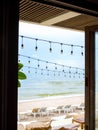 Hanging festive string wired light bulbs decorate under the roof outside the cafe on beachfront with seascape view background. Royalty Free Stock Photo