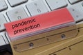 Hanging folder with red tab on which pandemic prevention is noted. A keyboard in the background